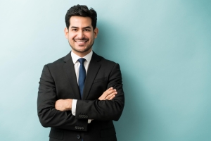 smiling-young-male-professional-standing-with-arms-crossed-while-making-eye-contact-against-isolated-background